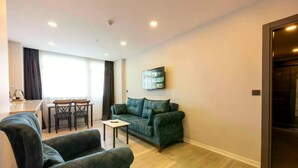 A modern living room with a sofa, two armchairs, a small table, and a dining area with a chair and table. - Venesia Hotel (Arsin)