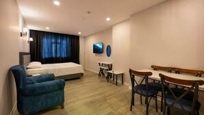 A hotel room with a bed, a blue armchair, a dining table with chairs, a TV, and a small table with a chair. - Venesia Hotel (Arsin)