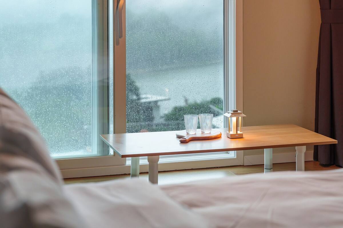 Un dormitorio con una cama, una mesita de noche con lámpara y una ventana con vistas al exterior.