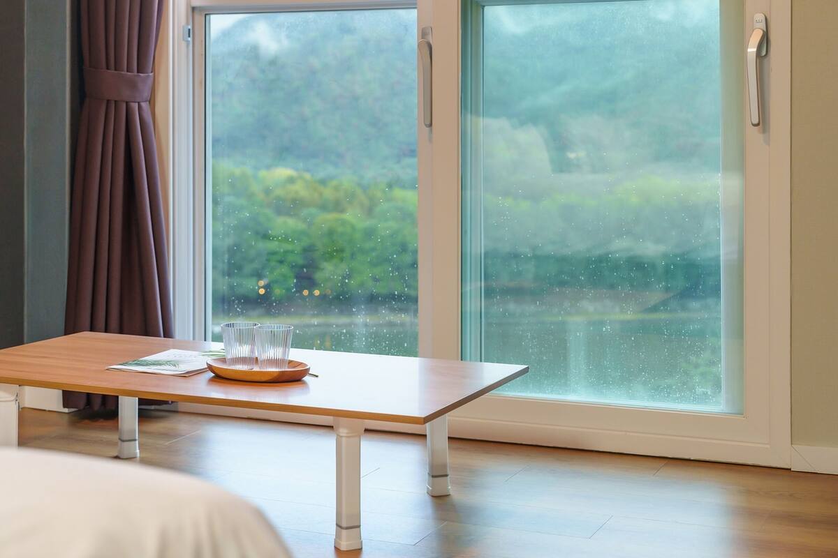 Una habitación con una mesa de madera, una cama y un ventanal con vistas a zonas verdes.
