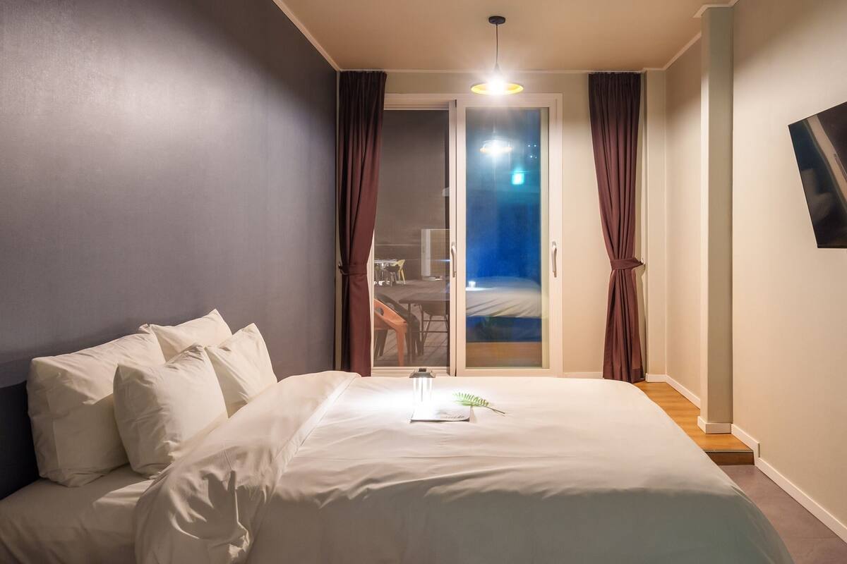 Habitación de hotel con cama, televisor montado en la pared y puerta corrediza que da a un balcón.