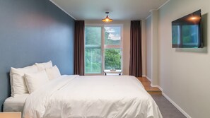 A bedroom with a large bed, a window with curtains, a table with a glass, and a mounted TV. - Viva Pension Nami Island, Gapyeong (Gapyeong)