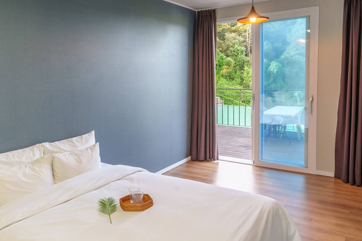Un dormitorio con cama, ventana con cortinas y vista a un espacio exterior.