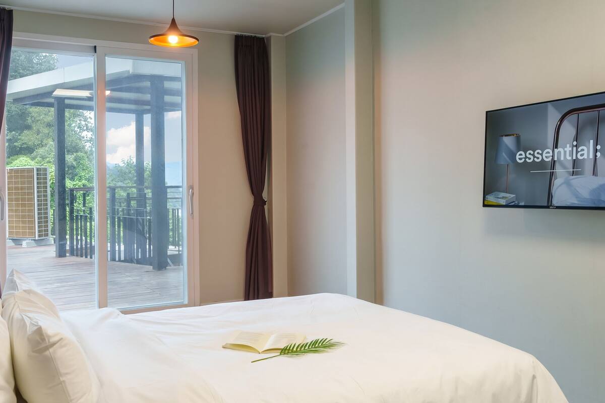 Un dormitorio con una cama, un televisor en la pared y vistas a una terraza exterior.