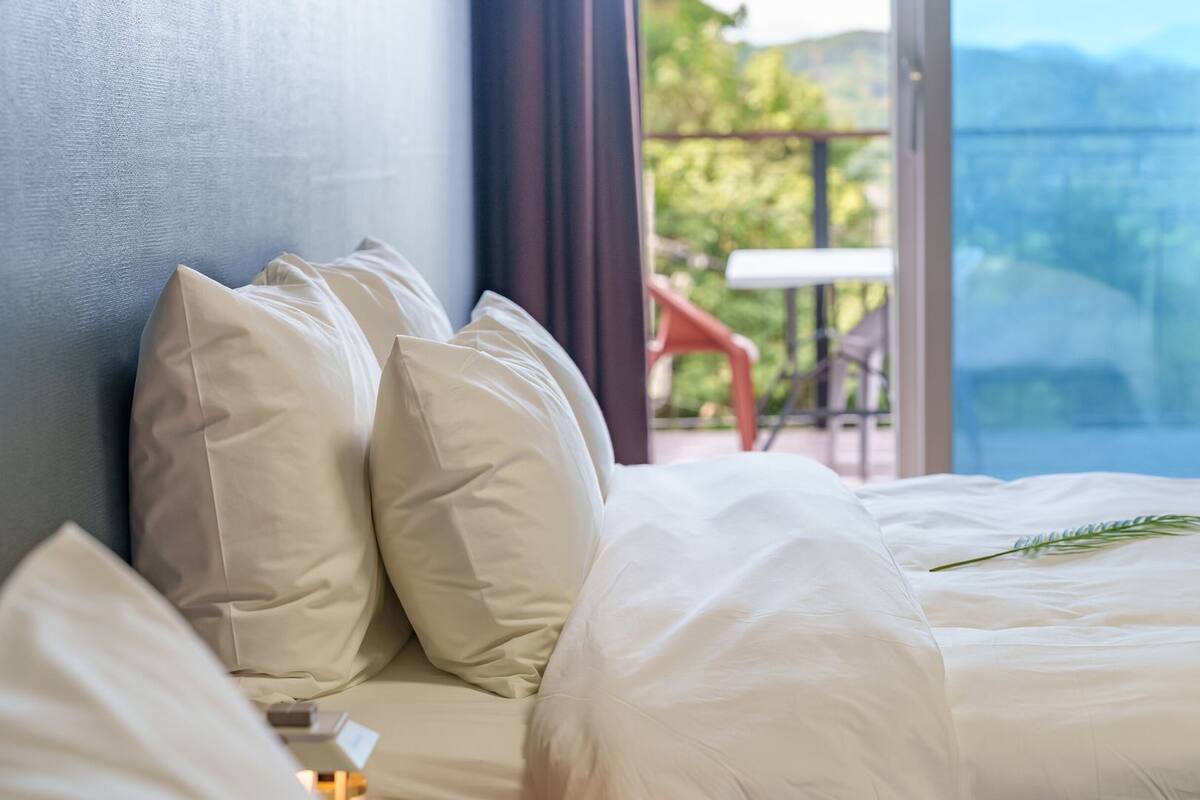 Una habitación de hotel con cama, almohadas y vistas a un balcón con mesa y sillas.