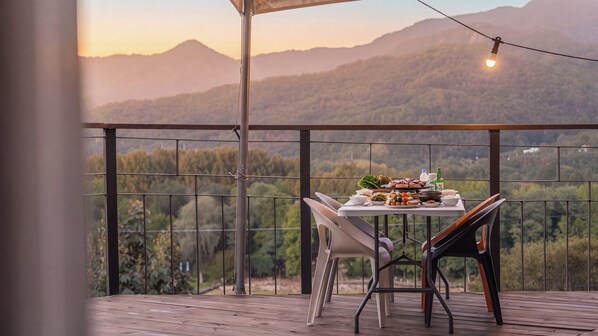 A balcony with a table set for dining, overlooking a mountainous landscape.