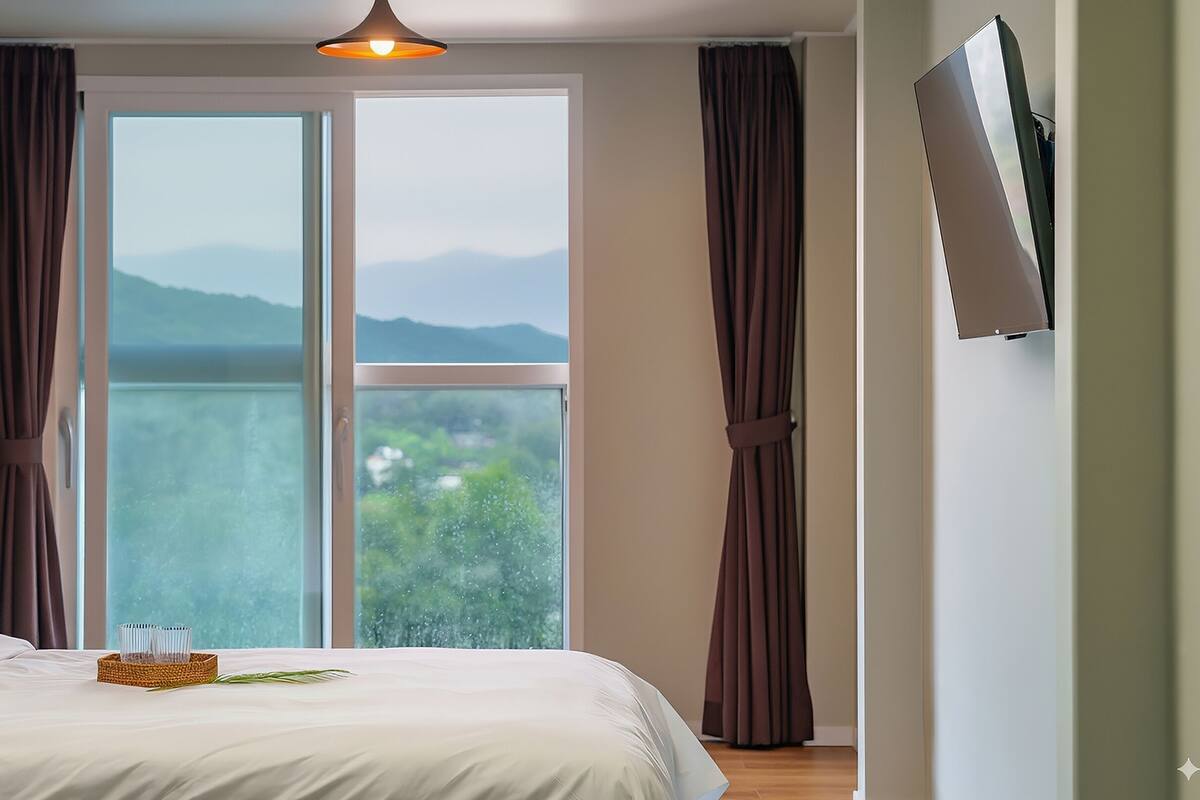 Un dormitorio con un ventanal grande, una cama, una mesita de noche y un televisor montado en la pared.