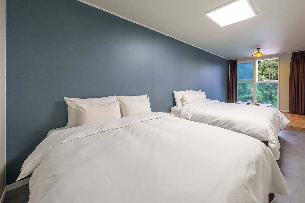 Una habitación con dos camas, un tragaluz, una ventana con cortinas y vistas al exterior.