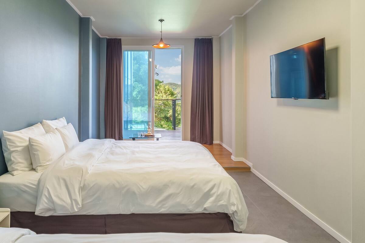 Una habitación de hotel moderna con una cama grande, un televisor de pantalla plana y un balcón con vistas a zonas verdes.