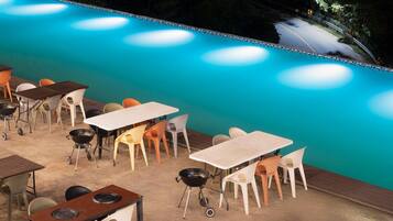 An outdoor pool area with multiple tables and chairs, surrounded by a concrete deck.