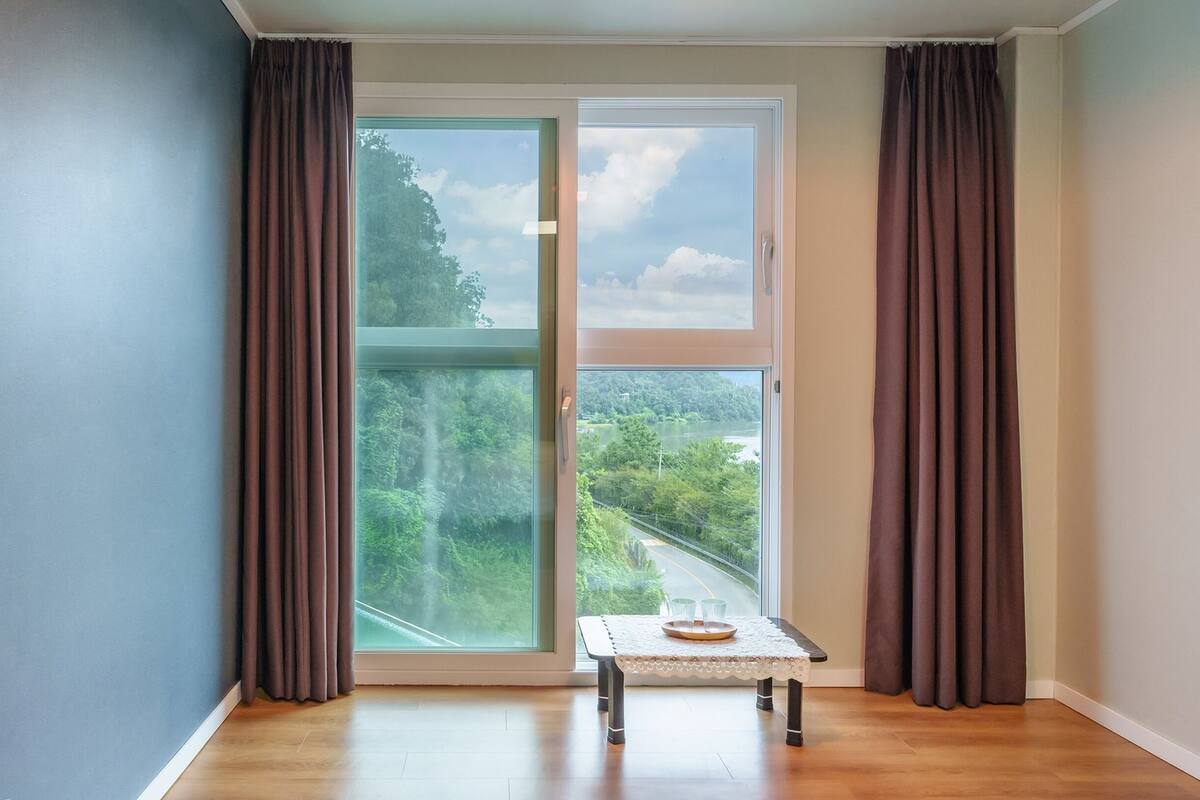 Una habitación con puerta de vidrio corrediza que da a un balcón, una mesita con bandeja y vistas a una calle y zonas verdes.