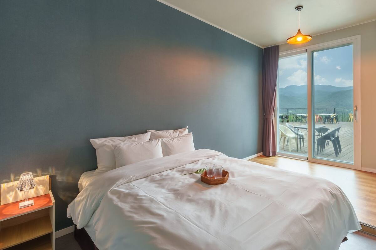 Un dormitorio con una cama grande, una mesita de noche con lámpara y vistas a una terraza con mobiliario exterior.