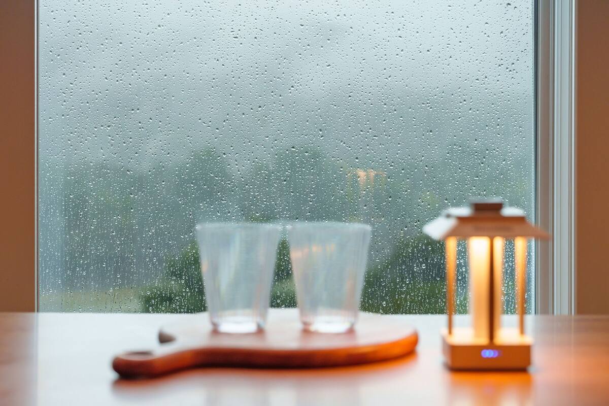 Una mesa con dos vasos transparentes y un posavasos de madera, y un farol encendido en un alféizar.
