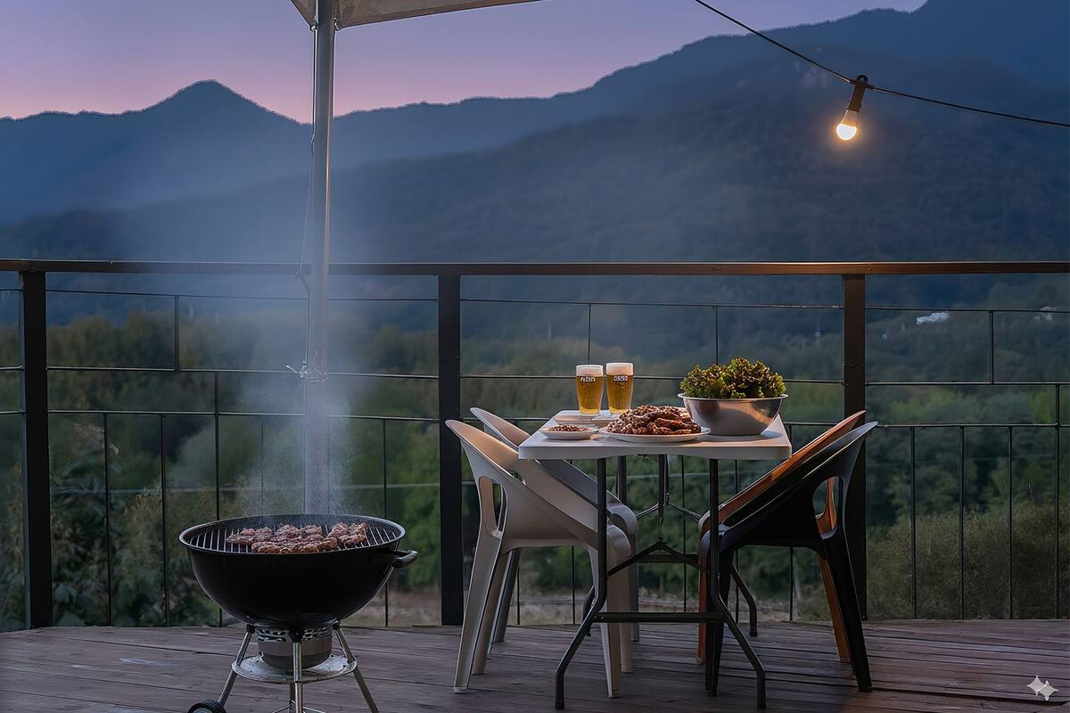 Un área de comedor al aire libre con una parrilla, mesa, sillas y vistas a las montañas.