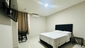 Una camera d'albergo moderna e pulita, con un letto, un tavolino, una TV a parete e un condizionatore d'aria.