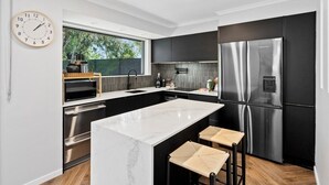 Una cocina moderna con una isla grande, electrodomésticos de acero inoxidable y vistas a la vegetación.