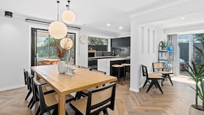 Una cocina moderna con una isla central, un comedor con mesa y sillas de madera, y un ventanal que proporciona luz natural.