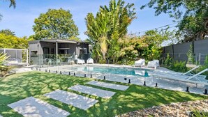 Un área de piscina moderna al aire libre, con una piscina cristalina, piedras como escalones y sillas de descanso.