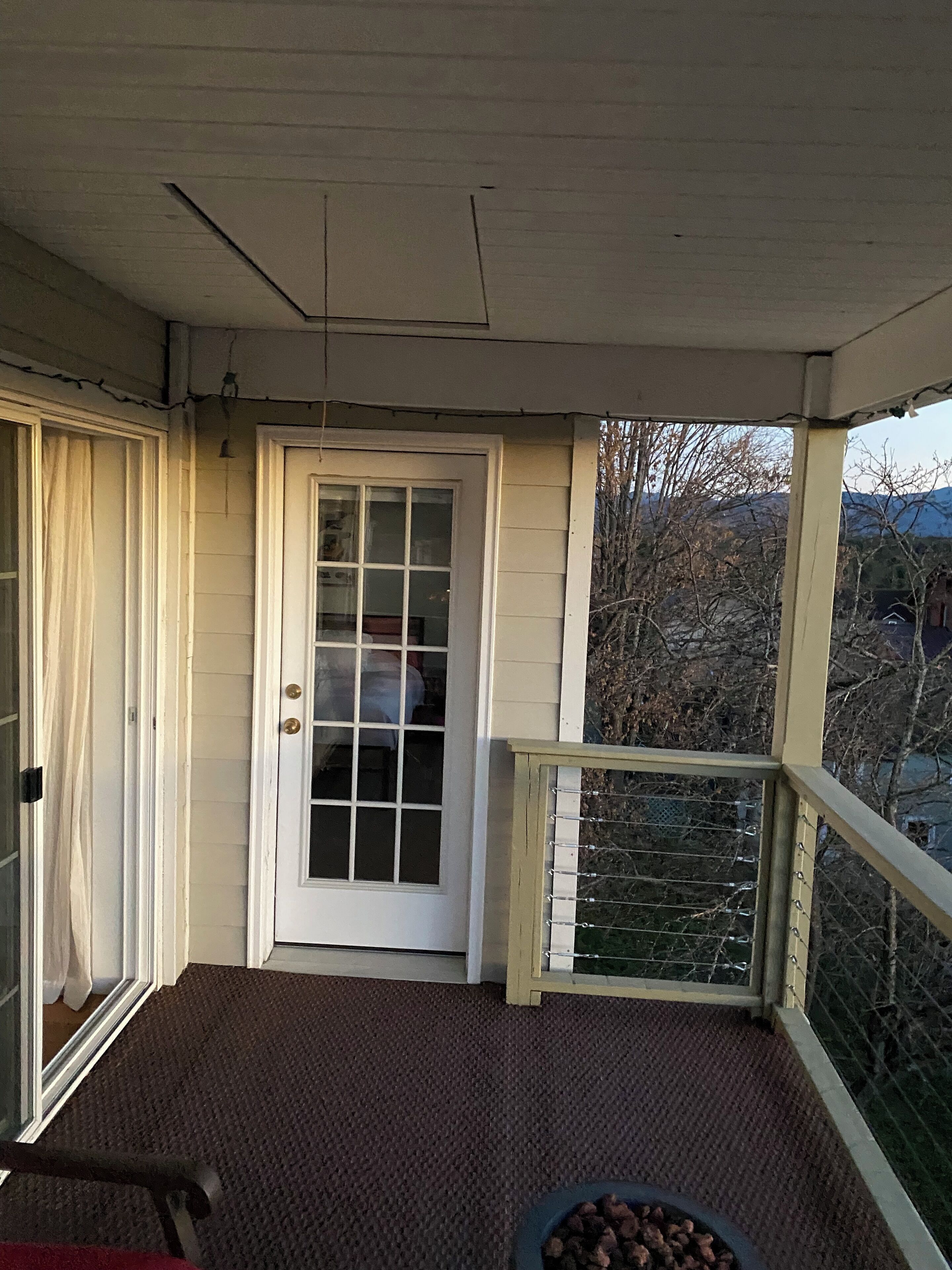 A porch with a door, a small table with a bowl, and a view of trees and mountains.
