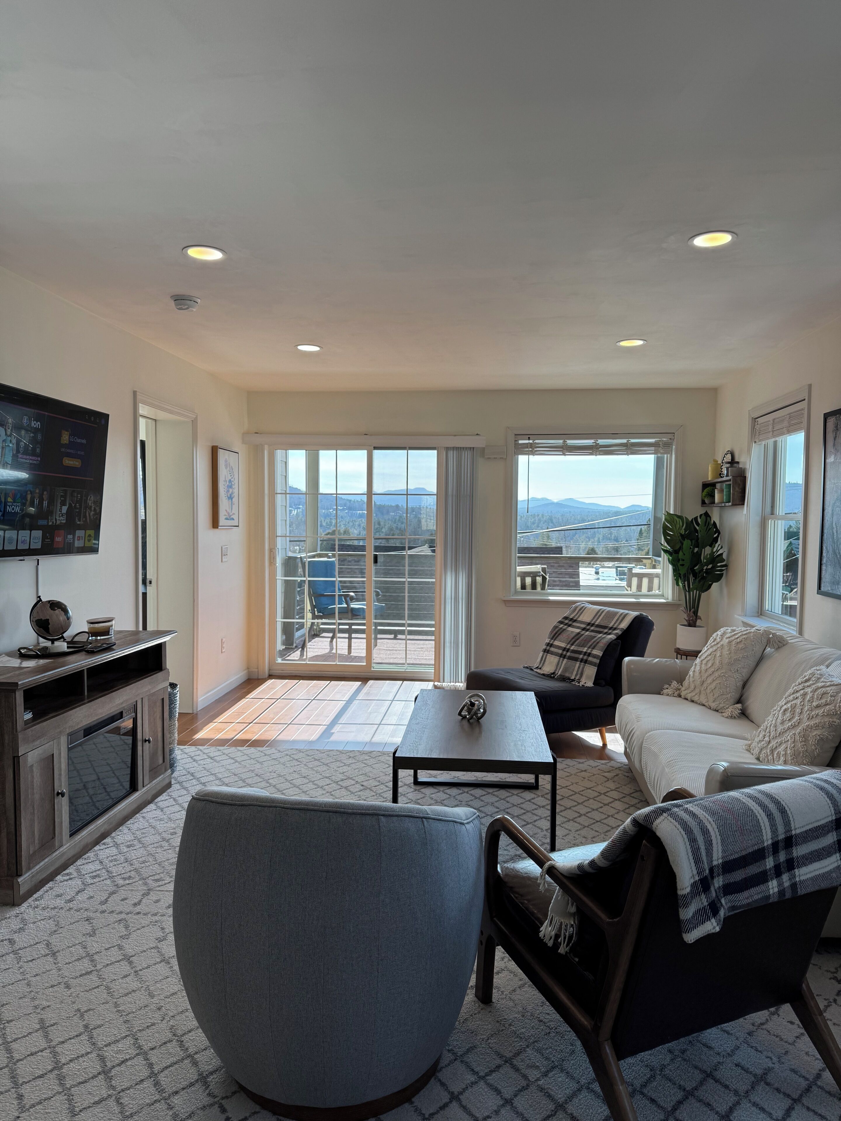 A spacious living room with a large window offering a city view, a flat-screen TV, and a comfortable seating area.