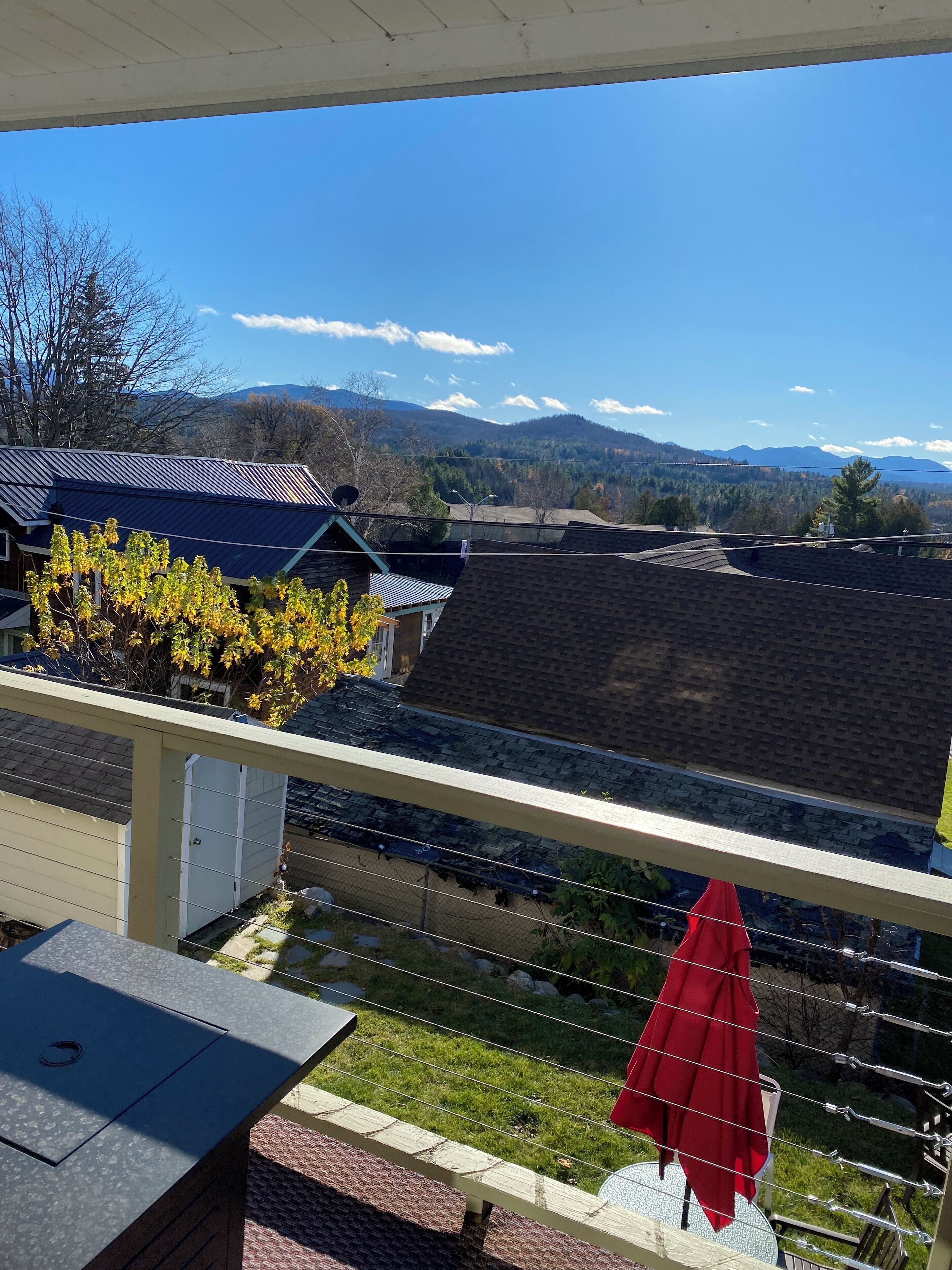 A balcony with a red umbrella, a view of houses, and mountains in the distance.