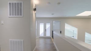 Un couloir avec un mur blanc, une grille d’aération, une porte et une fenêtre.