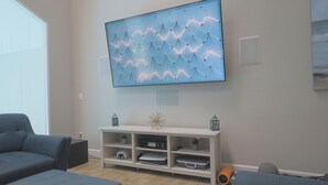 Un salon moderne doté d’un grand téléviseur à écran plat fixé au mur, d’un meuble de rangement blanc en dessous et de deux canapés de couleur foncée.