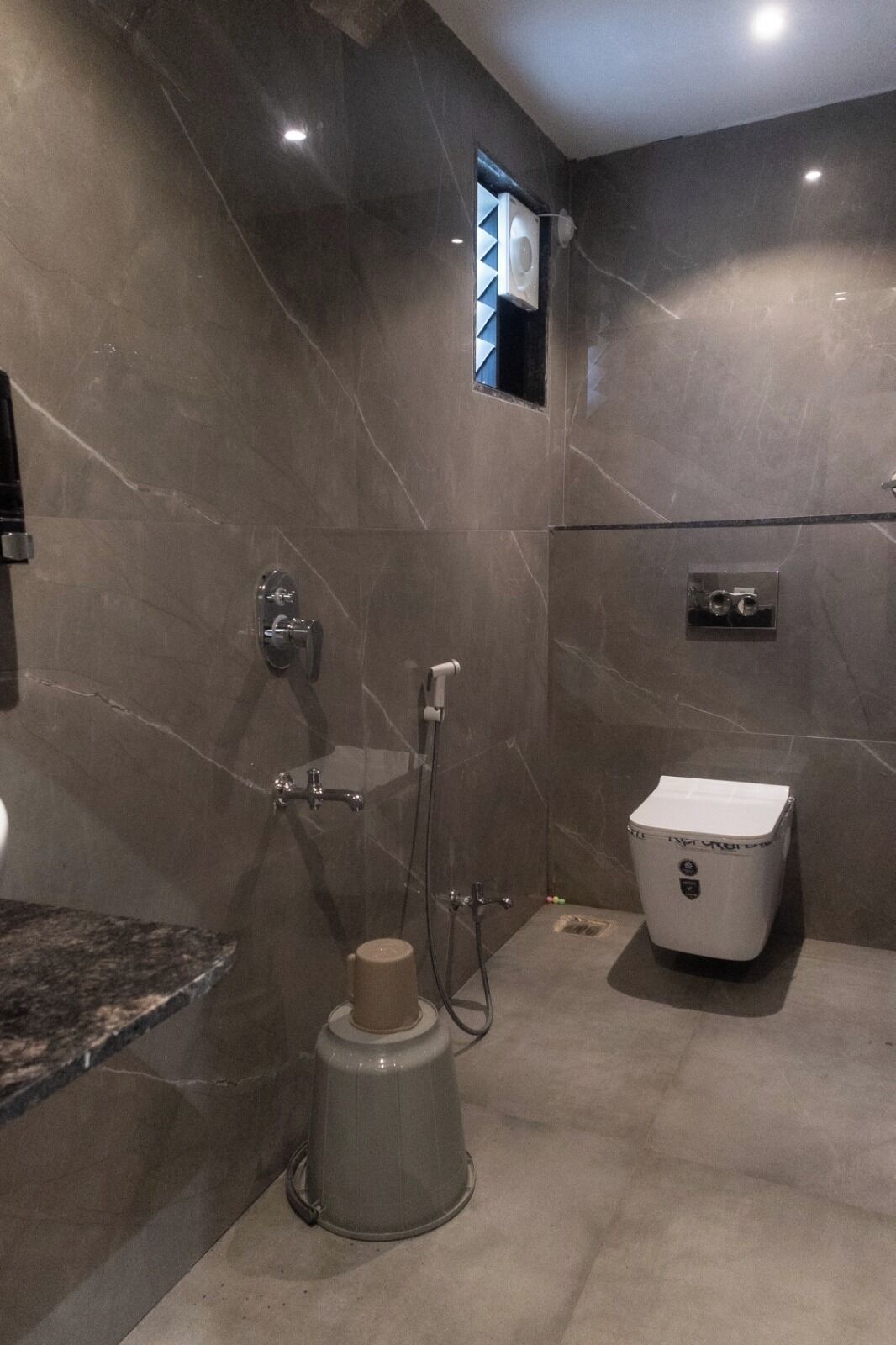 Une salle de bain moderne avec un mur en marbre, une douche, des toilettes et un lavabo.