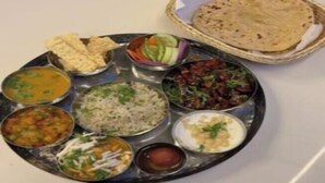 A traditional Indian meal with various dishes on a metal plate, including rice, curry, and flatbread, served on a table. - Sukoon Prestige Palace (Bhopal)