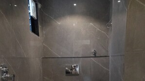 A modern bathroom with a marble floor, a built-in toilet, a shower area, and a small shelf with toiletries. - Sukoon Prestige Palace (Bhopal)