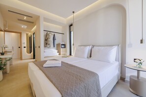 Een moderne hotelkamer met een groot bed, een nachtkastje, een ronde spiegel en een klein rond tafeltje met een bloemenvaas.