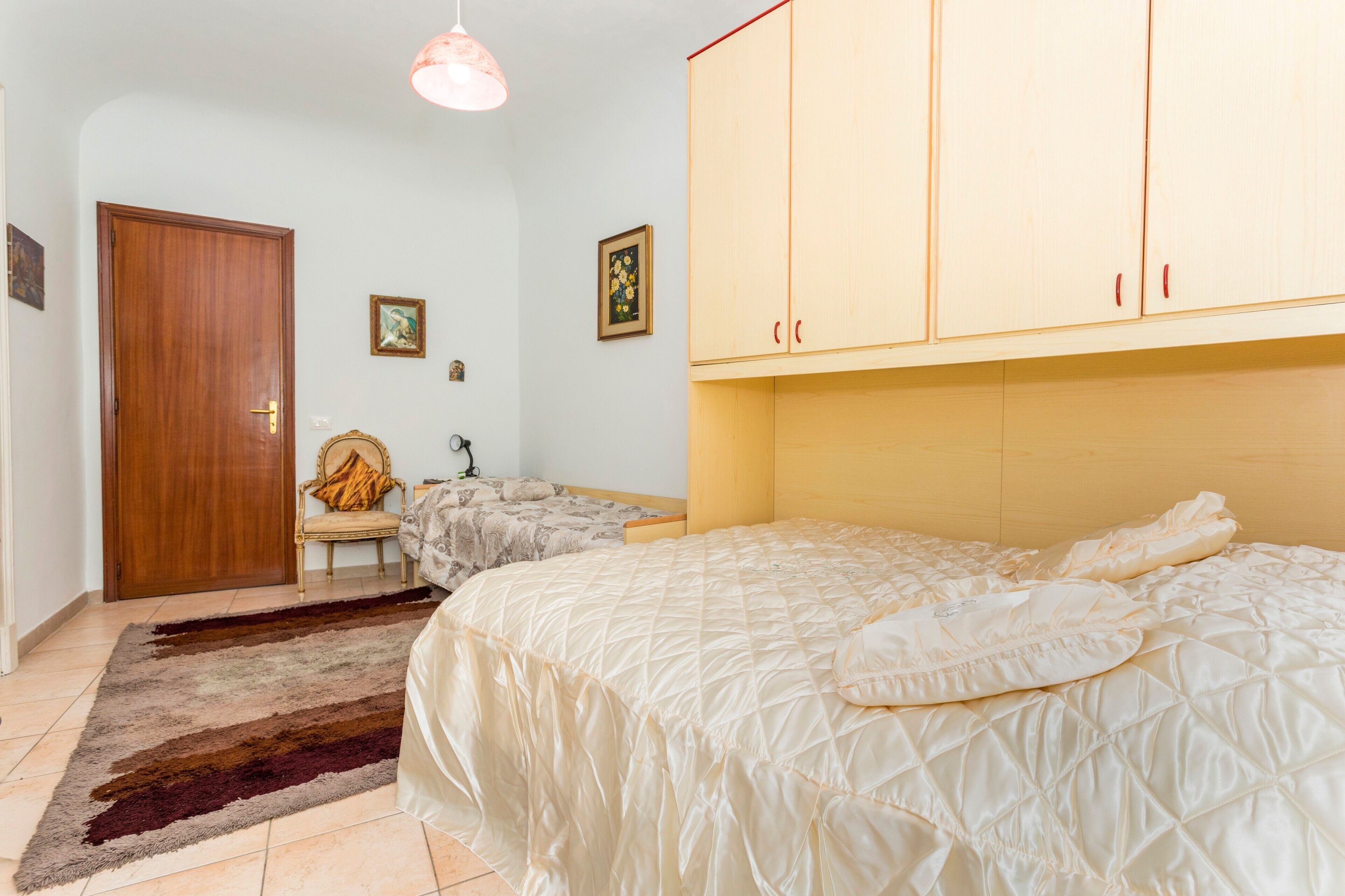 A bedroom with a bed, a wardrobe, a chair, a rug, and a door.