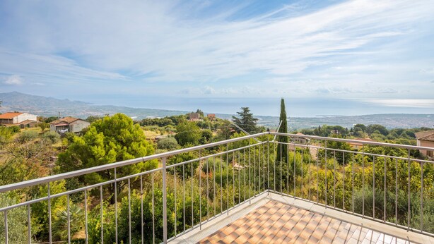 Une terrasse offrant une vue sur un paysage vallonné, avec des maisons et des arbres.