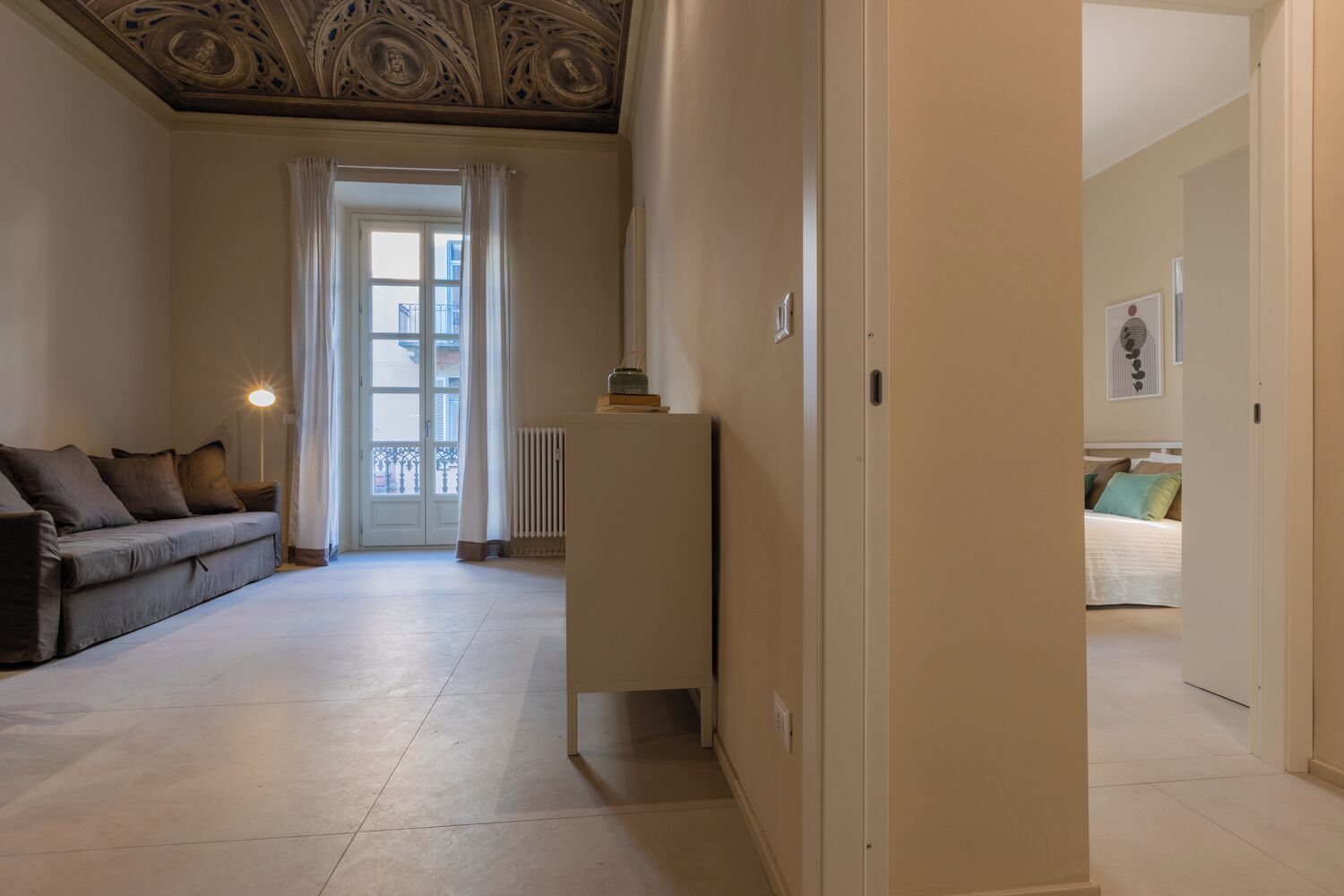 Un soggiorno spazioso con un divano, un termosifone e una porta che dà su una camera da letto.