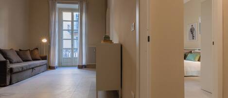 Un soggiorno spazioso con un divano, un termosifone e una porta che dà su una camera da letto.