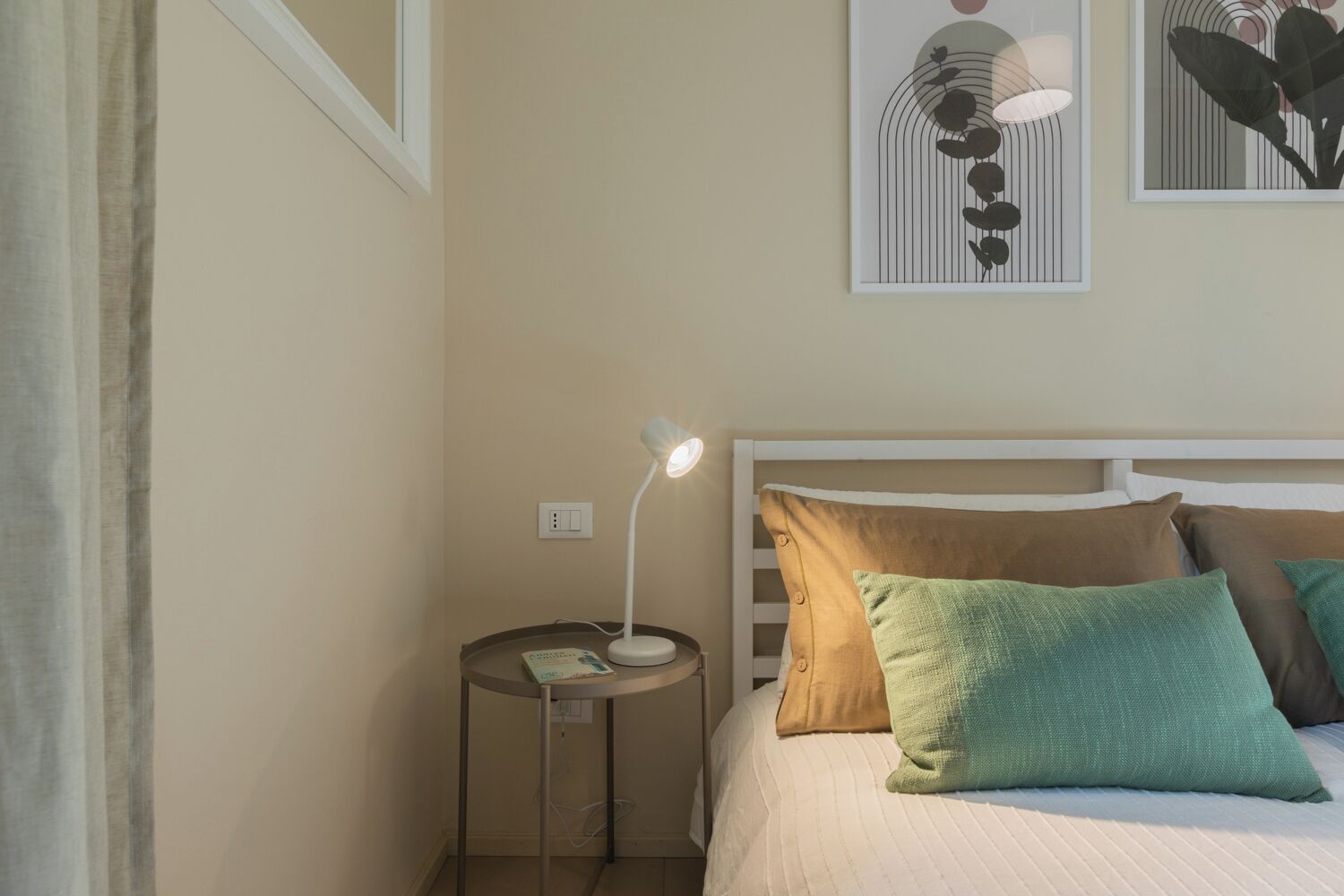 A bedroom with a bed, pillows, a bedside table with a lamp, and framed artwork on the wall.