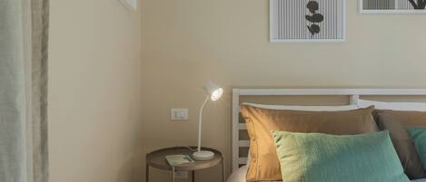 A bedroom with a bed, pillows, a bedside table with a lamp, and framed artwork on the wall.