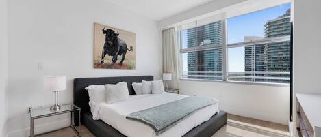 A modern bedroom with a large bed, a city view, and a bull painting on the wall.