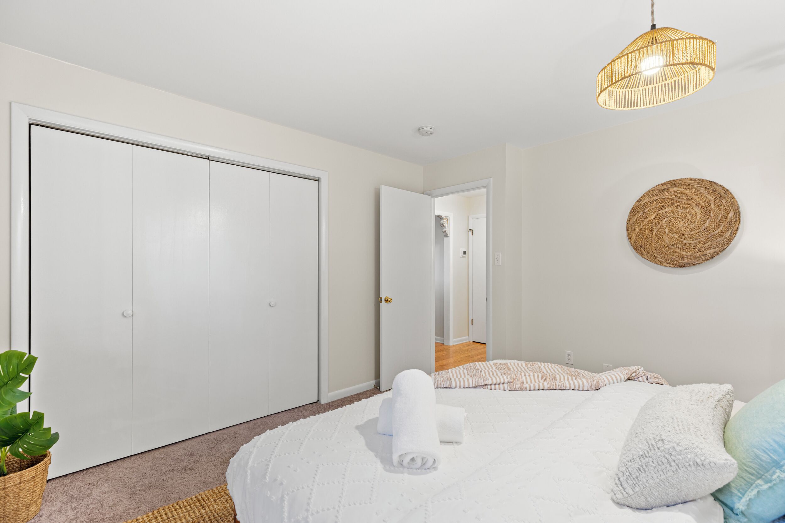 Un dormitorio con un armario grande, una cama con ropa de cama blanca, un tapiz de pared tejido y una lámpara colgante.