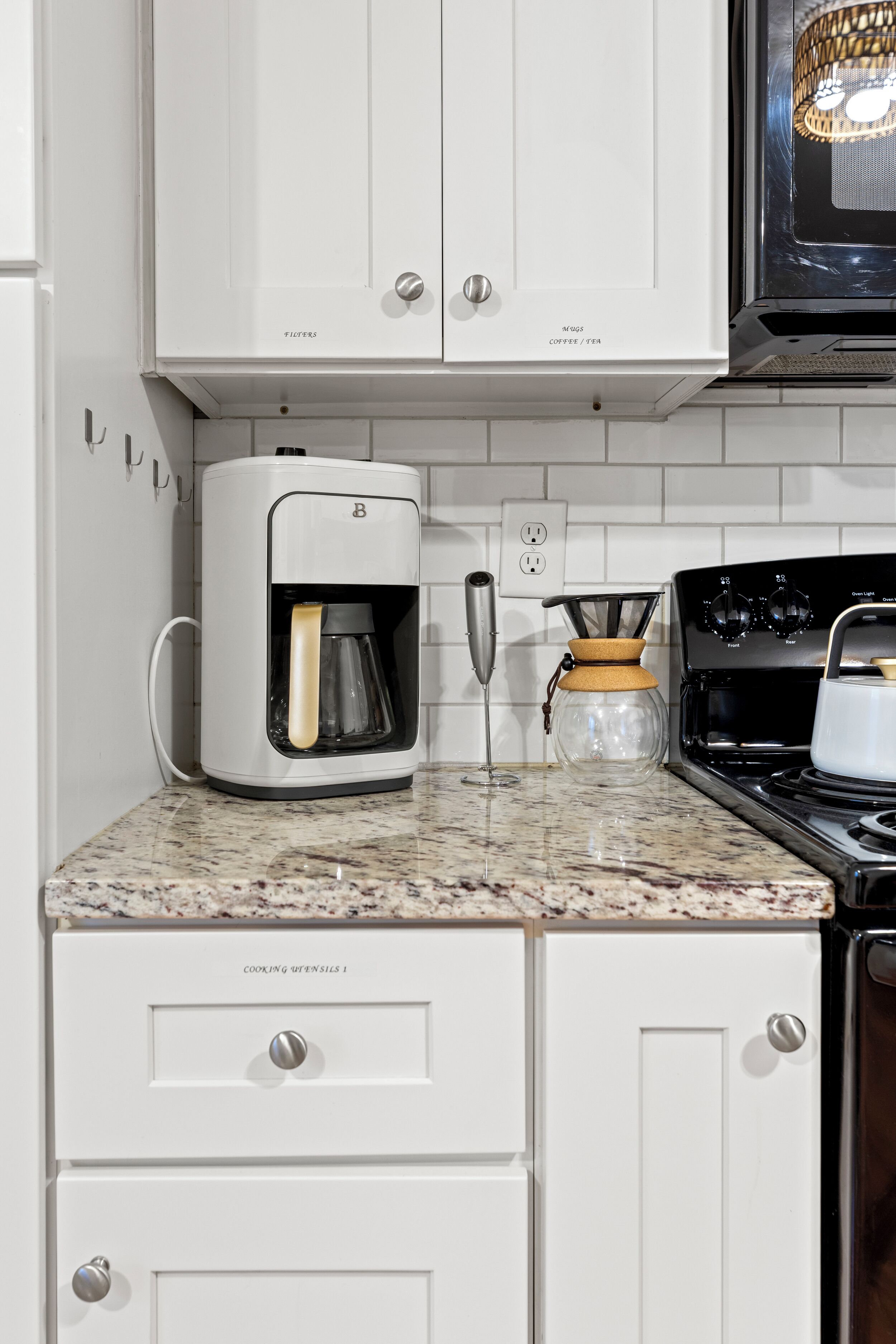 A kitchen with white cabinets, a coffee maker, a kettle, and a stove.