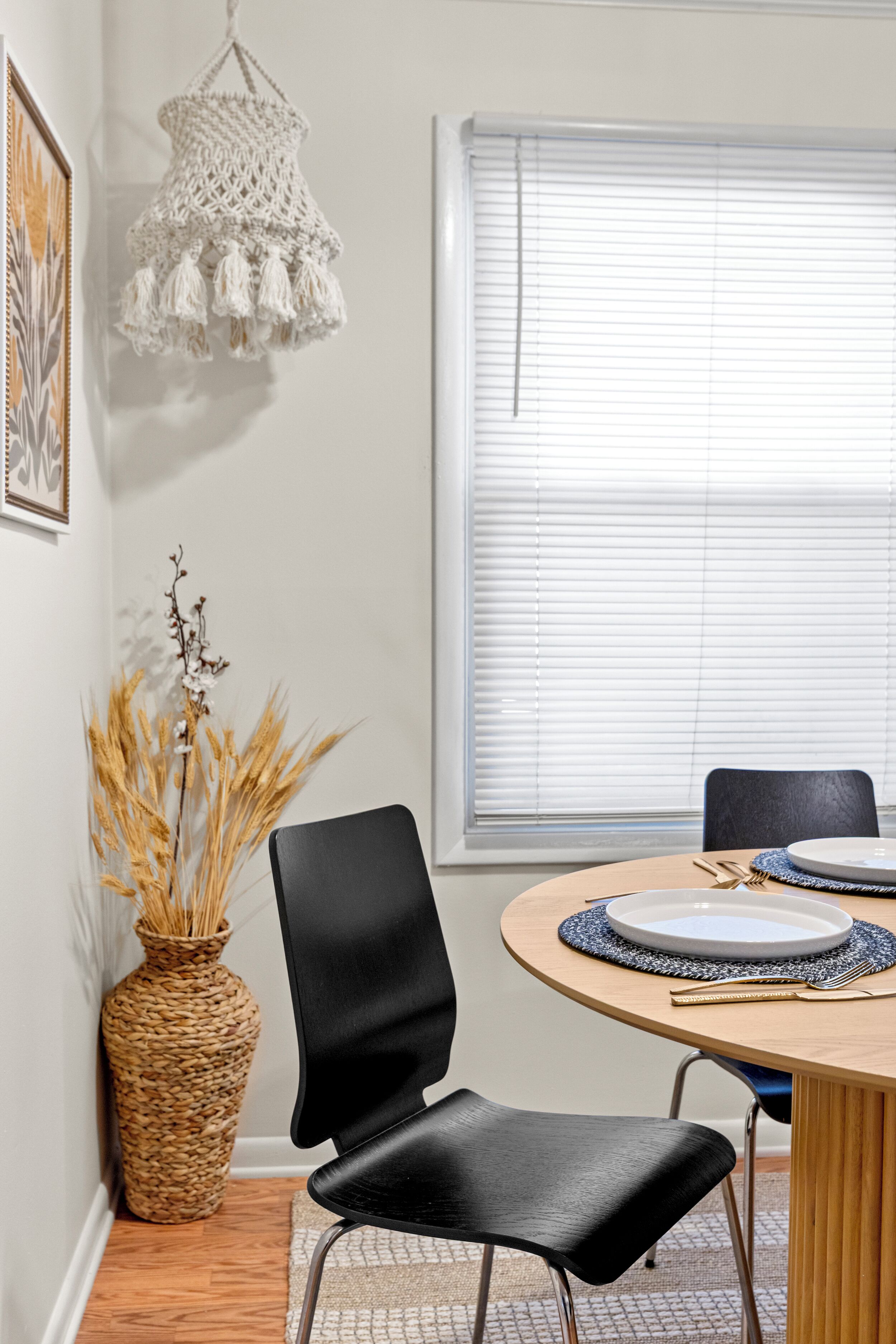 Ein Essbereich mit einem runden Tisch, schwarzen Stühlen, einer gewebten Vase mit getrockneten Pflanzen und einer Makramee-Lampe.