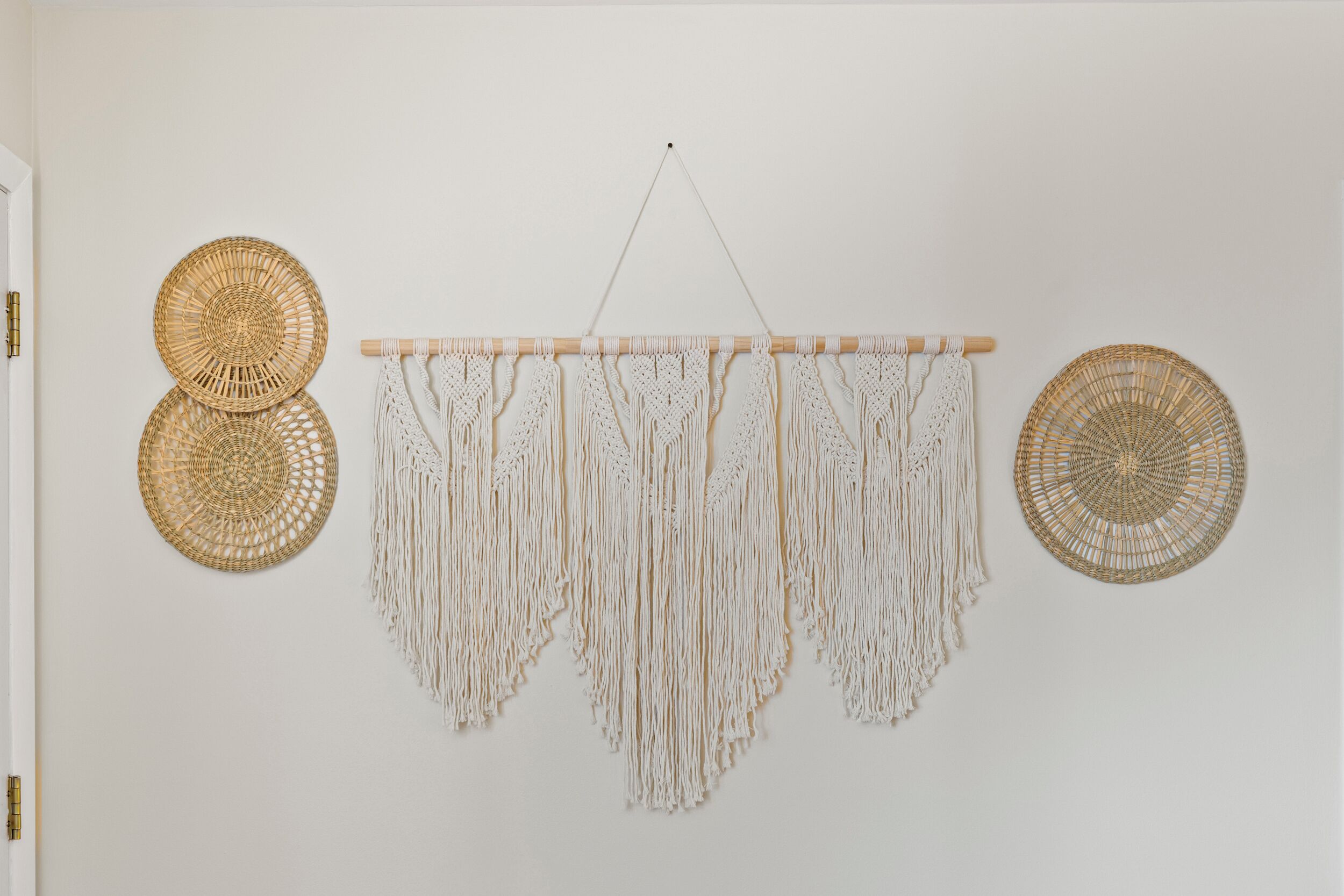 A wall with three macramé wall hangings and two woven wall decorations.