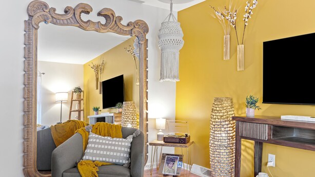 A living room with a large mirror, a sofa with cushions, a television, and decorative items on a wooden console.