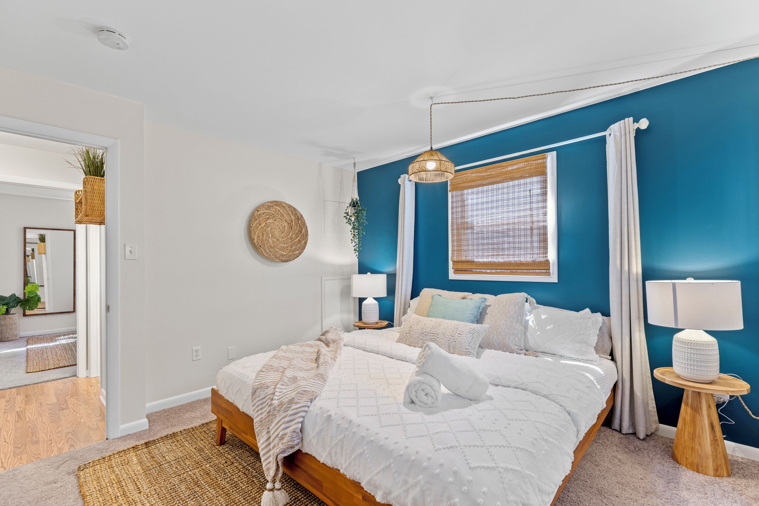 Quarto com cama, mesas de cabeceira, janela com cortinas e um espelho.