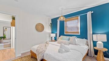 Quarto com cama, mesas de cabeceira, janela com cortinas e um espelho.