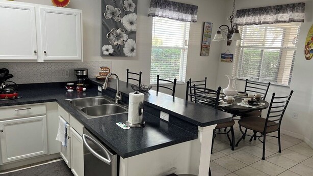A kitchen with white cabinets, a black countertop, and a dining area with a table and chairs.