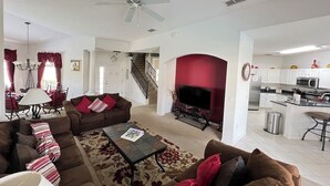 A spacious living room with a sofa set, a coffee table, and a fireplace. There is a kitchen area with modern appliances visible in the background.