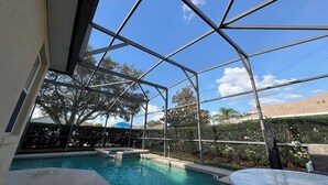A covered outdoor swimming pool with a clear view of the surrounding trees and a distant building.