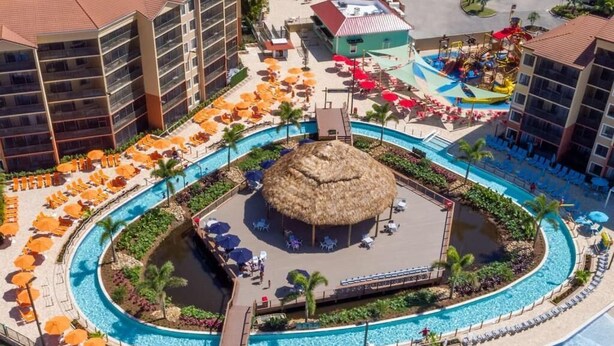 A resort with a central pool, sun loungers, a thatched-roof bar area, and a water slide. - Wesgate Lakes Resort (Orlando)