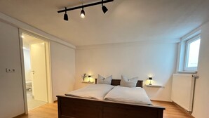 A bedroom with a wooden bed, bedside lamps, a window, and a door leading to another room. - Friendly warm apartment between Alb and Rems incl. sauna (Böbingen)